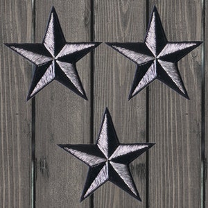 May include: Three black and silver five-pointed stars on a wooden background.