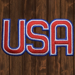 May include: A red, white and blue embroidered patch with the word "USA" in a bold, blocky font.