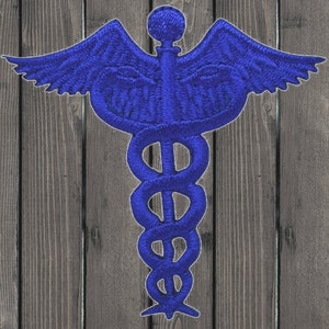 May include: A blue embroidered medical symbol with a snake wrapped around a staff and wings. The symbol is on a wooden background.