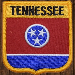 以下が含まれることがあります： 黄色い背景に黒い文字で「TENNESSEE」と書かれた、赤、白、青の刺繍パッチ。パッチの中央には、3つの白い星が描かれた青い円があります。