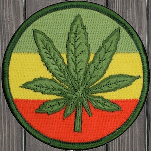 May include: A green marijuana leaf embroidered on a circular patch with red, yellow, and green stripes.