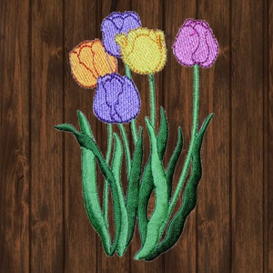Op de afbeelding: Borduurwerk van een boeket met vijf tulpen met groene stelen en bladeren. De tulpen zijn paars, geel en roze.