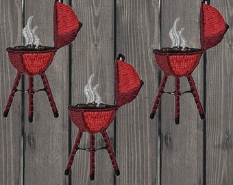 May include: Three red and black barbecue grills with lids open and smoke coming out of the top. The grills are on a wooden background.