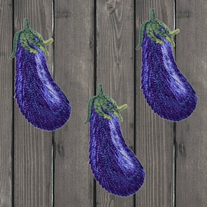 May include: Three purple and green embroidered eggplant patches on a wood background.