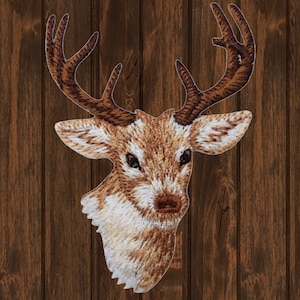Könnte beinhalten: Gestickter Aufnäher mit dem Kopf eines braunen Hirsches mit großen Geweih. Der Hirsch hat eine weiße Schnauze und einen hellbraunen Körper.
