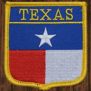 May include: A blue, red, and white embroidered patch with a single white star and the word "TEXAS" in yellow lettering. The patch is surrounded by a yellow border.