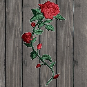 Puede incluir: Rosa roja bordada con hojas y tallo verdes. La rosa está sobre un fondo de madera.