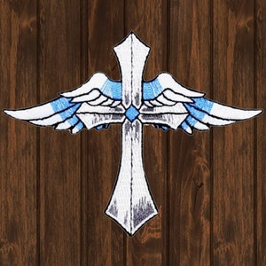 May include: A white cross with blue and white wings, embroidered on a brown wooden background.