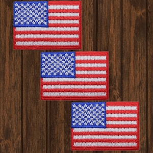 Puede incluir: Tres parches bordados de la bandera estadounidense sobre un fondo de madera. Las banderas son rojas, blancas y azules con estrellas blancas sobre un campo azul.