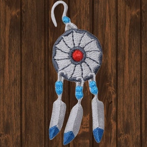 以下が含まれることがあります： 白い羽根飾りで、赤い中心と青い羽根が付いている。羽根飾りは木製の表面に吊り下げられている。