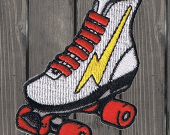 Puede incluir: Patín de ruedas blanco con ruedas rojas y un diseño de rayo amarillo. El patín tiene cordones rojos y una lengüeta blanca.