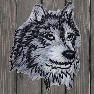 May include: A black and white embroidered patch of a wolf's head. The wolf is looking to the right with its mouth slightly open. The fur is detailed with black and white stitching.