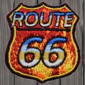 Puede incluir: Parche bordado de la Ruta 66 con forma de escudo. El parche presenta las palabras "ROUTE 66" en letras blancas sobre el número "66" en azul y amarillo. El fondo es rojo, amarillo y naranja.
