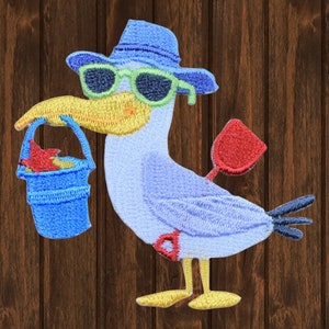 May include: Embroidered patch of a cartoon seagull wearing sunglasses and a blue hat, holding a blue bucket and a red shovel. The seagull is light blue with a yellow beak and feet.