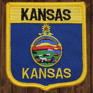 May include: A blue and yellow embroidered patch with the state seal of Kansas and the word "KANSAS" written twice in yellow.