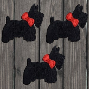 Può includere: Tre toppe ricamate nere a forma di cane Scottish Terrier, ciascuna con un papillon rosso brillante. Le toppe sono dettagliate con cuciture visibili e sono su uno sfondo di legno.
