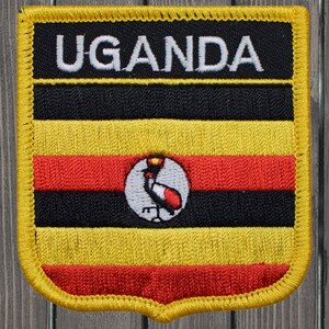 Könnte beinhalten: Ein gestickter Aufnäher mit der Flagge von Uganda. Der Aufnäher ist gelb, schwarz, rot und weiß mit einem Kranich in der Mitte. Die Worte "UGANDA" sind oben auf dem Aufnäher in weiß gestickt.