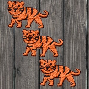 Könnte beinhalten: Drei orangefarbene, gestickte Bügelbilder von Tigern. Die Tiger sind cartoonartig und haben schwarze Streifen.