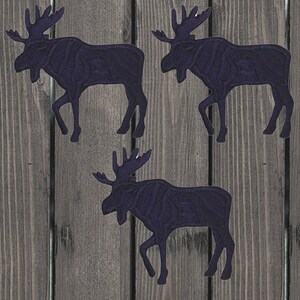 May include: Three black silhouette moose cutouts on a woodgrain background.