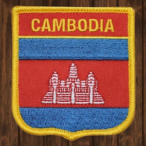 May include: A blue, red, and white embroidered patch with the word "CAMBODIA" in yellow lettering. The patch features the Cambodian flag with a white temple design.