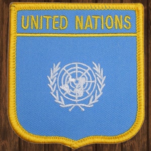 May include: A blue patch with a yellow border and the words "UNITED NATIONS" in yellow lettering. The patch features a white emblem of the United Nations, which includes a world map surrounded by olive branches.