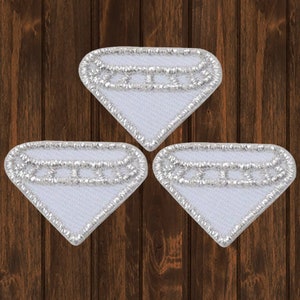 May include: Three white diamond-shaped patches with silver stitching. The patches are sewn with a silver thread around the edges and have a silver line across the centre.