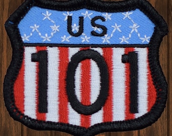 May include: Embroidered patch in the shape of a shield, featuring the text "US 101". The top portion is light blue with white stars, and the bottom has red and white stripes. The patch is outlined in black.