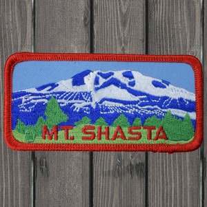 May include: A red, white, and blue embroidered patch with the words "MT. SHASTA" in green. The patch features a mountain with snow on the top.
