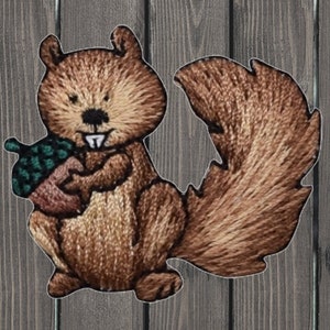 May include: An embroidered squirrel holding an acorn, with a green top and brown base. The squirrel has a bushy tail and a friendly expression.