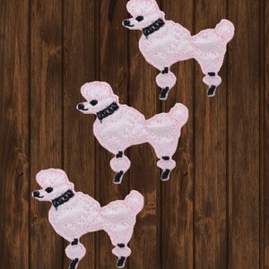 May include: Three pink poodle dog iron-on patches with black collars and a dotted pattern.