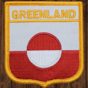 May include: A red, white, and yellow embroidered patch with the word "GREENLAND" in yellow lettering and the flag of Greenland in the center.