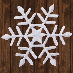 May include: White felt snowflake ornament with a six-pointed star design. The snowflake is against a brown wood background.