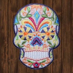 Peut inclure: Écusson brodé en forme de tête de mort mexicaine, orné de motifs floraux et géométriques aux couleurs vives. Le patch a une base blanche et une bordure bleu foncé, idéal pour les vêtements ou accessoires.