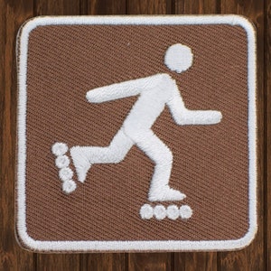 May include: A brown square patch with a white outline and a white silhouette of a person roller skating. The person is facing right and has a simple stick figure design. The roller skates have four wheels each.