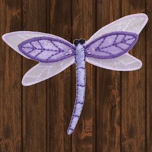 May include: A purple dragonfly with clear wings and a beaded body. The dragonfly is embroidered and has a detailed design.