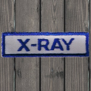 以下が含まれることがあります： 青い縁取りのある白い長方形のパッチで、青い刺繍で「X-RAY」と書いてあります。