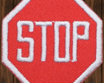 Könnte beinhalten: Rotes achteckiges Stoppschild mit weißem Rand und weiß gesticktem Text "STOP".