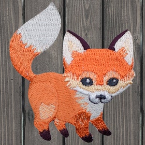 May include: Embroidered orange fox patch with a white tipped tail. The fox is standing on all four paws with its head tilted slightly to the side. The patch is perfect for adding a touch of whimsy to clothing, bags, or other crafts.