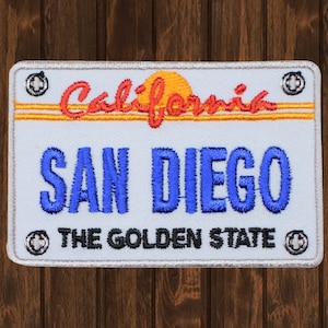 May include: White embroidered patch with red "California" text and a yellow sunset graphic above. The text "SAN DIEGO" is in blue below the state name. The text "THE GOLDEN STATE" is in black below the city name.