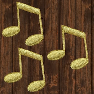 Könnte beinhalten: Vier goldene Notensymbole vor einem dunkelbraunen Holzmaserungshintergrund. Die Noten haben ein strukturiertes, metallisches Aussehen, was auf ein dekoratives oder gesticktes Design hindeutet. Geeignet für Musik-Themen-Bastelarbeiten oder Dekoration.