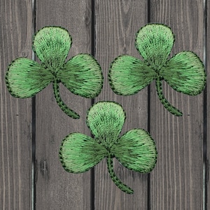 May include: Three green felt shamrock patches on a wooden background.