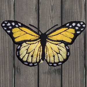 May include: A yellow butterfly with black and white markings on a wooden background.