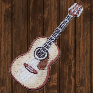 May include: A brown and white embroidered patch of an acoustic guitar. The guitar has a brown body, a white pickguard, and a brown neck with black strings.