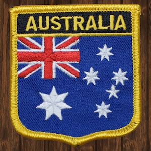 Op de afbeelding: Een blauwe en witte geborduurde patch met het woord "AUSTRALIA" in gele letters op een zwarte achtergrond. De patch toont de Australische vlag met de Union Jack in de linkerbovenhoek en een sterrenbeeld van zeven witte sterren op een blauwe achtergrond.