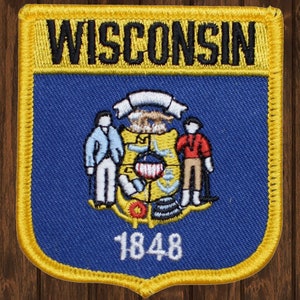 Peut inclure: Un écusson brodé bleu et jaune avec le sceau de l'État du Wisconsin. Le sceau représente deux personnages debout de chaque côté d'un bouclier avec l'année 1848 en dessous. L'écusson porte le mot "WISCONSIN" en lettres noires en haut.