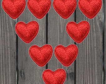 May include: Nine red felt hearts arranged in a triangular pattern on a wooden background.