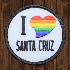 Könnte beinhalten: Weißer gestickter Aufnäher mit schwarzem Rand. Der Aufnäher zeigt ein Regenbogenherz mit dem Text "I love Santa Cruz".