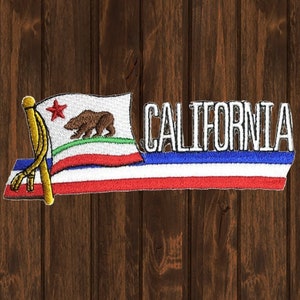 Puede incluir: Parche bordado con la bandera del estado de California con una estrella roja, un oso marrón y rayas verdes y blancas. La palabra "CALIFORNIA" está bordada en blanco sobre una pancarta con rayas rojas, blancas y azules.