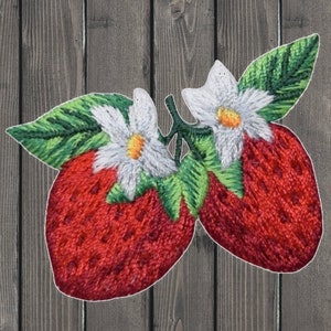 May include: Embroidered patch featuring two red strawberries with white flowers and green leaves. The strawberries have a textured appearance, and the flowers have yellow centers. The patch is outlined in white.