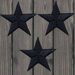 May include: Three black embroidered star patches on a wooden backdrop. Each star features five points and a textured look, indicating a stitched design. The stars are evenly spaced, creating a balanced composition.
